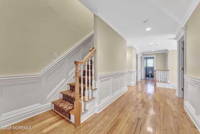 hallway with a wainscoted wall, a decorative wall, and light wood finished floors