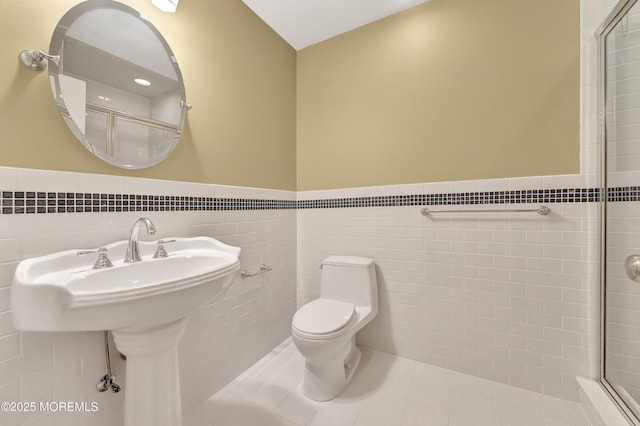 bathroom featuring toilet, a wainscoted wall, tile walls, tile patterned floors, and a shower with door