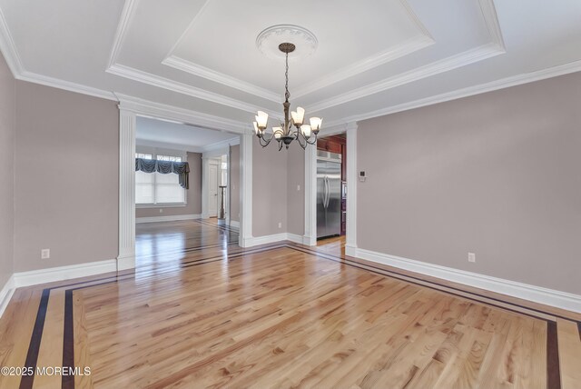 spare room featuring a notable chandelier, a raised ceiling, and wood finished floors