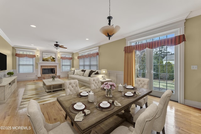 dining area featuring light wood-type flooring, a glass covered fireplace, wainscoting, and crown molding