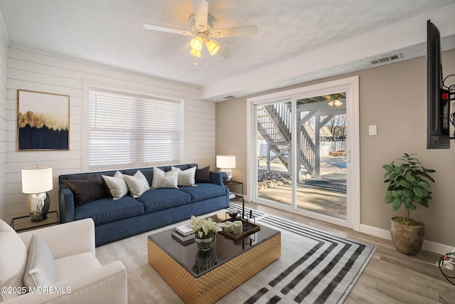 living room featuring light hardwood / wood-style floors, a textured ceiling, ceiling fan, and wooden walls