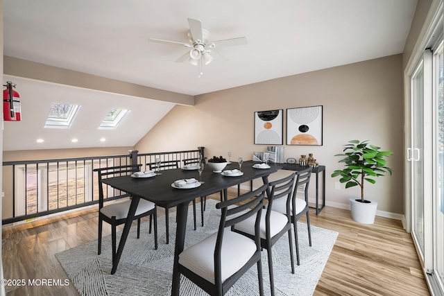 dining room with light wood-type flooring, ceiling fan, and vaulted ceiling with skylight