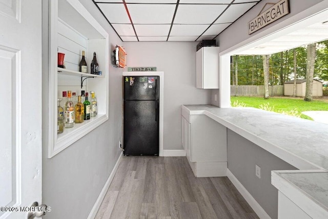 interior space with black refrigerator, white cabinets, a drop ceiling, and wood-type flooring