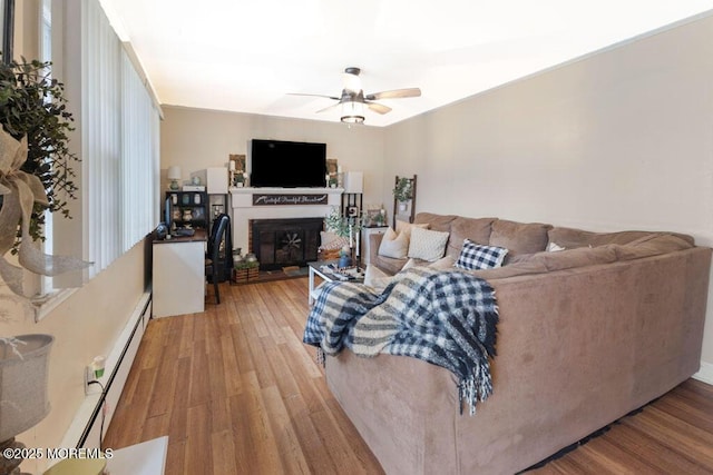 living room with ceiling fan, a baseboard heating unit, and hardwood / wood-style floors