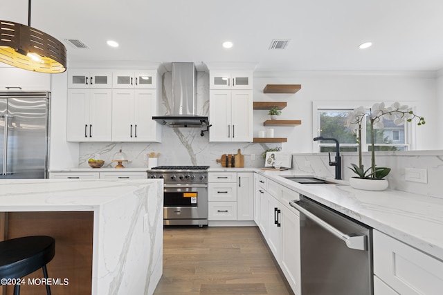 kitchen with premium appliances, decorative light fixtures, wall chimney exhaust hood, white cabinets, and sink