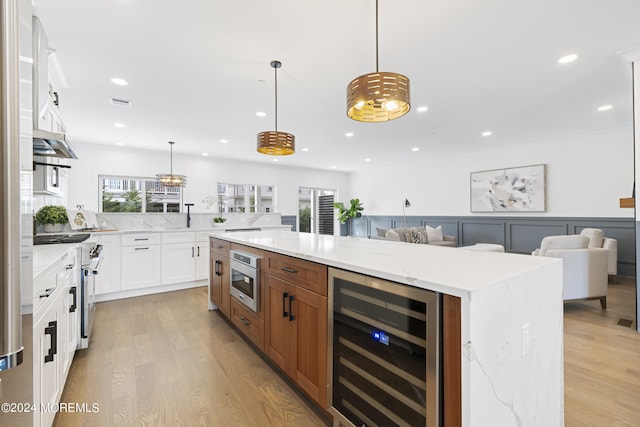 kitchen with hanging light fixtures, light stone countertops, a large island, white cabinets, and beverage cooler