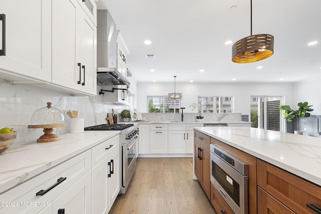 kitchen with pendant lighting, white cabinets, appliances with stainless steel finishes, tasteful backsplash, and light stone counters