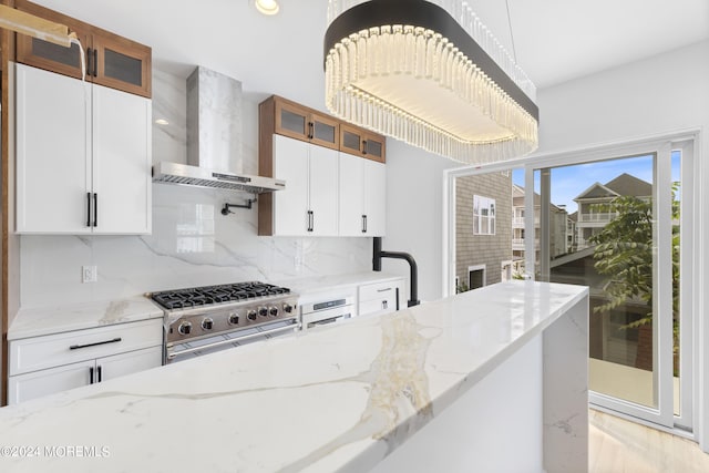 kitchen featuring light stone countertops, white cabinets, wall chimney range hood, stainless steel appliances, and tasteful backsplash