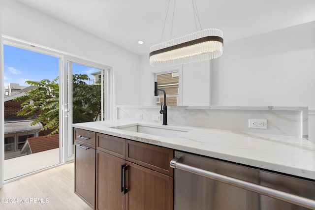 kitchen with pendant lighting, dishwasher, light hardwood / wood-style floors, sink, and light stone counters