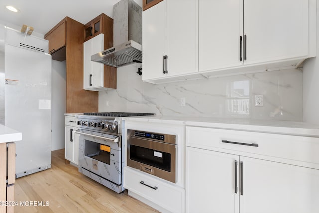 kitchen with appliances with stainless steel finishes, wall chimney exhaust hood, white cabinetry, and tasteful backsplash