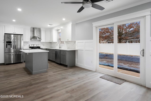 kitchen with ceiling fan, a center island, appliances with stainless steel finishes, gray cabinetry, and wall chimney exhaust hood