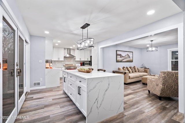 kitchen featuring a kitchen island, pendant lighting, white cabinets, wall chimney exhaust hood, and range