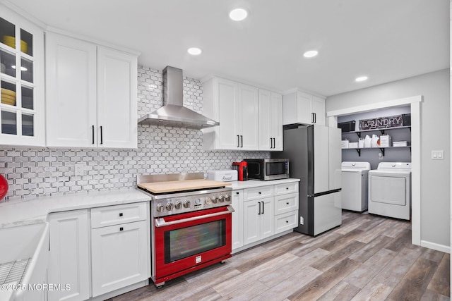 kitchen featuring refrigerator, wall chimney range hood, washing machine and clothes dryer, white cabinets, and range