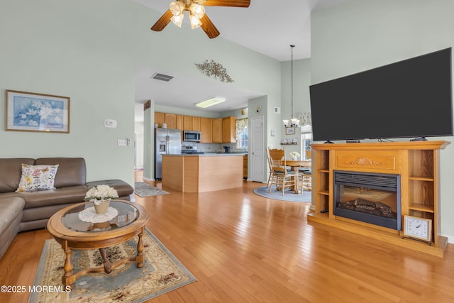 living room featuring a towering ceiling, ceiling fan with notable chandelier, and light wood-type flooring