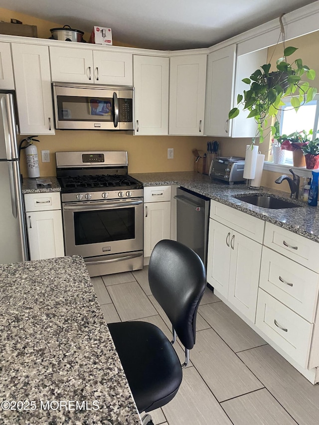 kitchen featuring white cabinetry, appliances with stainless steel finishes, sink, and dark stone counters