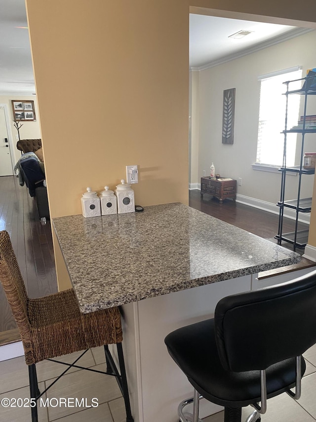 kitchen featuring crown molding, tile patterned floors, a breakfast bar, and kitchen peninsula