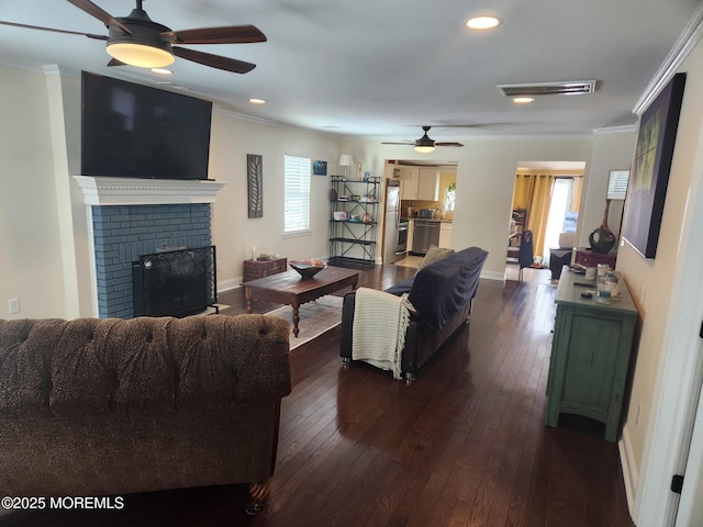 living room featuring crown molding, plenty of natural light, dark wood-type flooring, and a brick fireplace