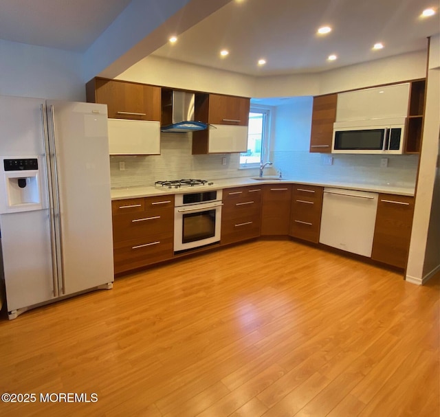 kitchen with wall chimney range hood, white appliances, sink, and light wood-type flooring