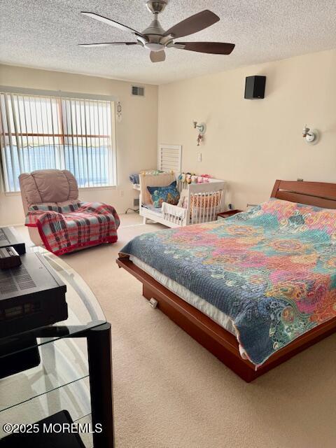 carpeted bedroom featuring ceiling fan and a textured ceiling