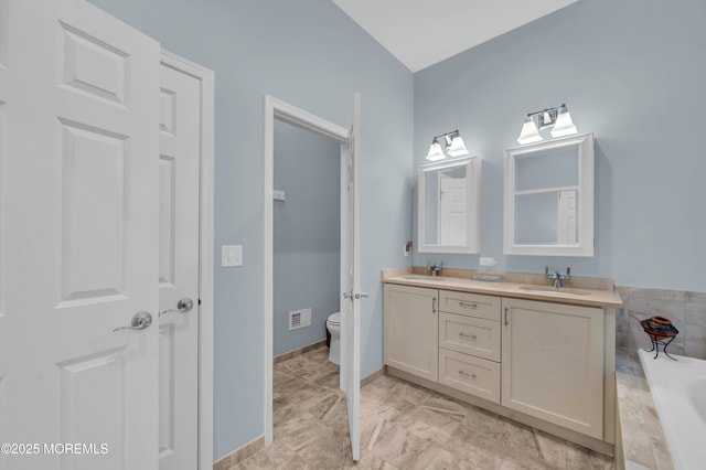 bathroom featuring toilet, tiled bath, and vanity