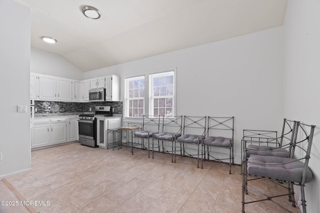 kitchen with white cabinets, appliances with stainless steel finishes, tasteful backsplash, and vaulted ceiling