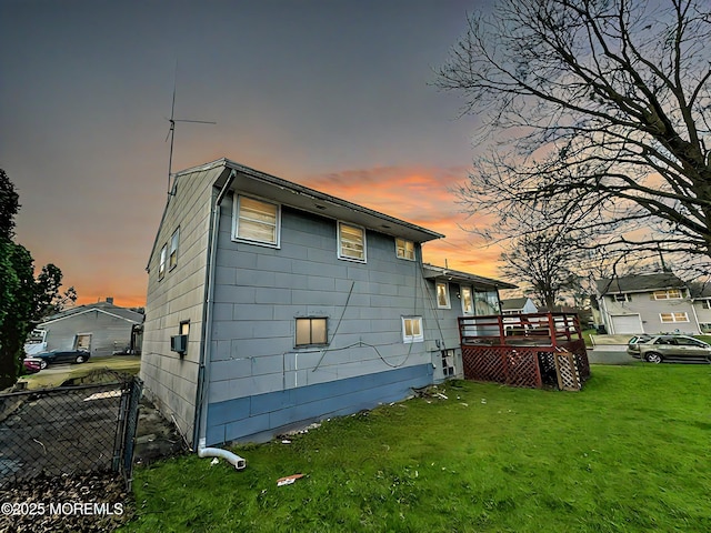 back house at dusk featuring a wooden deck and a yard