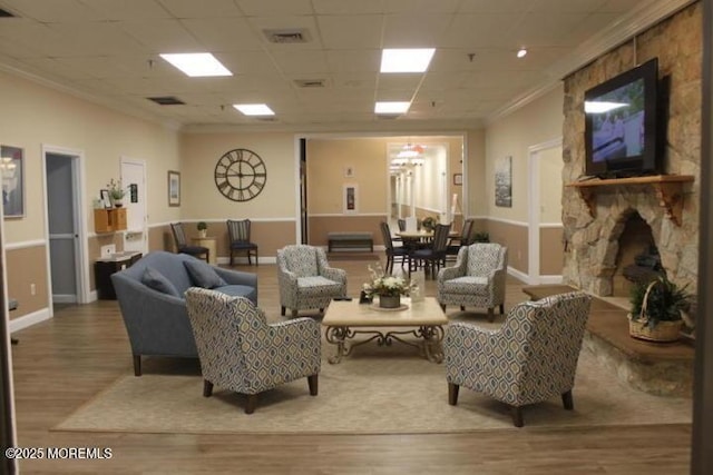 living room with hardwood / wood-style flooring, a fireplace, a drop ceiling, and crown molding