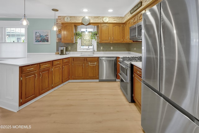 kitchen featuring pendant lighting, sink, backsplash, stainless steel appliances, and light hardwood / wood-style flooring