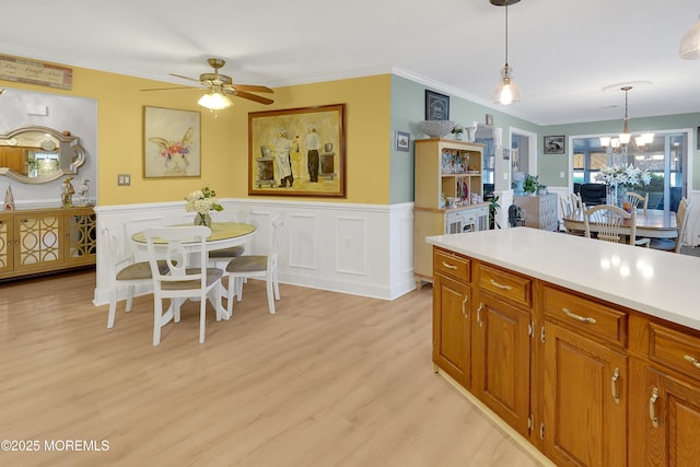 kitchen featuring hanging light fixtures, crown molding, ceiling fan with notable chandelier, and light hardwood / wood-style floors