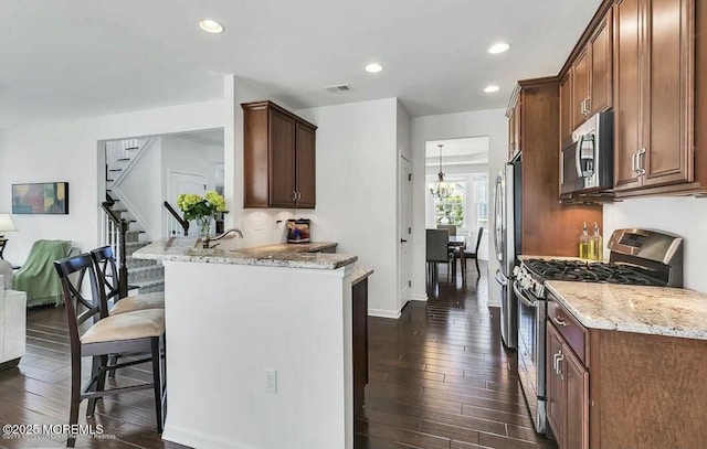 kitchen with kitchen peninsula, a breakfast bar, stainless steel appliances, light stone counters, and dark hardwood / wood-style floors