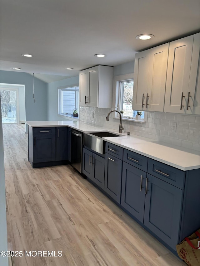 kitchen featuring kitchen peninsula, decorative backsplash, stainless steel dishwasher, light hardwood / wood-style flooring, and sink