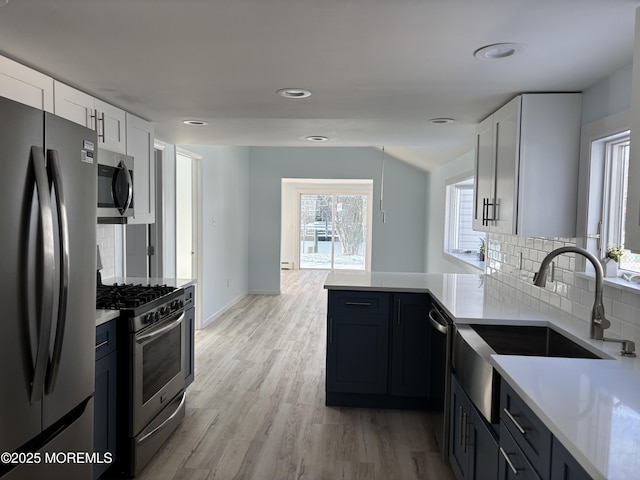 kitchen featuring backsplash, light hardwood / wood-style floors, kitchen peninsula, appliances with stainless steel finishes, and white cabinets