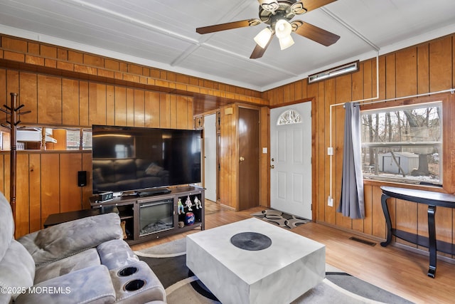 living room featuring ceiling fan, light hardwood / wood-style flooring, and wood walls