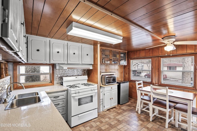 kitchen featuring appliances with stainless steel finishes, wood walls, sink, white cabinets, and wood ceiling