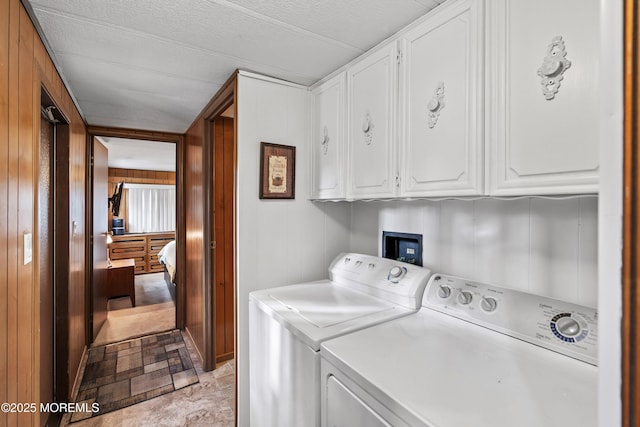 laundry area featuring cabinets, wooden walls, and separate washer and dryer