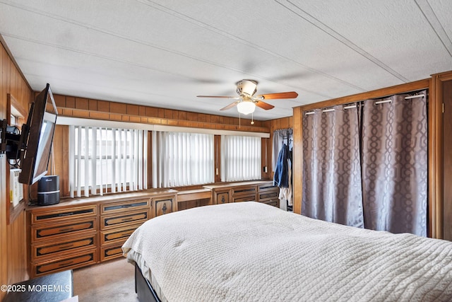 bedroom featuring light carpet, ceiling fan, wooden walls, and a textured ceiling