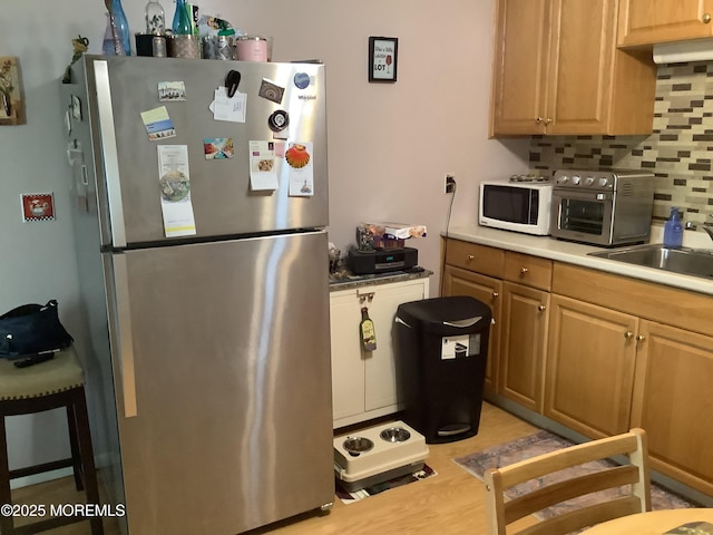 kitchen with sink, decorative backsplash, stainless steel refrigerator, and light hardwood / wood-style floors