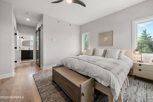 bedroom with multiple windows, ceiling fan, ensuite bathroom, light hardwood / wood-style flooring, and a barn door