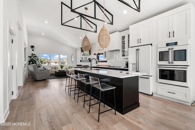 kitchen with sink, white cabinetry, white appliances, a breakfast bar, and an island with sink