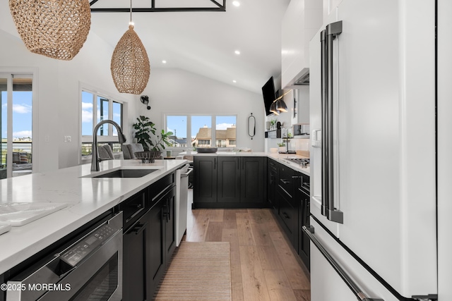 kitchen with light hardwood / wood-style flooring, vaulted ceiling, hanging light fixtures, high end white fridge, and sink