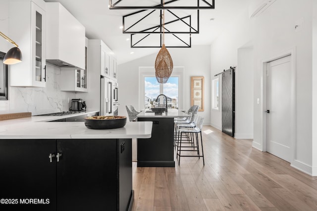 kitchen with a center island, white cabinetry, a barn door, custom range hood, and backsplash