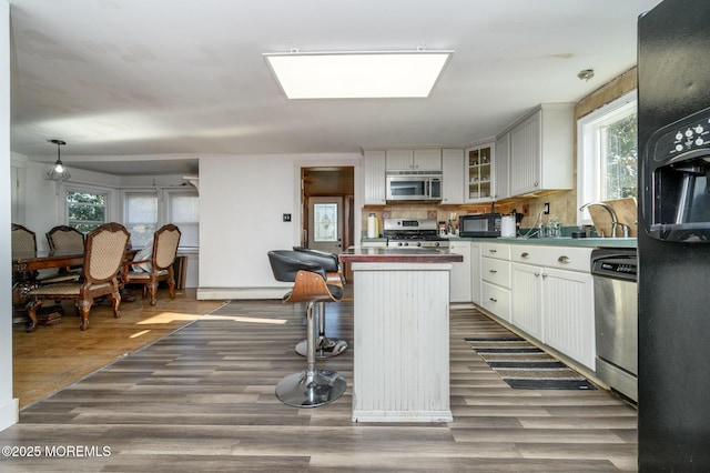 kitchen with decorative backsplash, hanging light fixtures, a baseboard heating unit, black appliances, and dark wood-type flooring