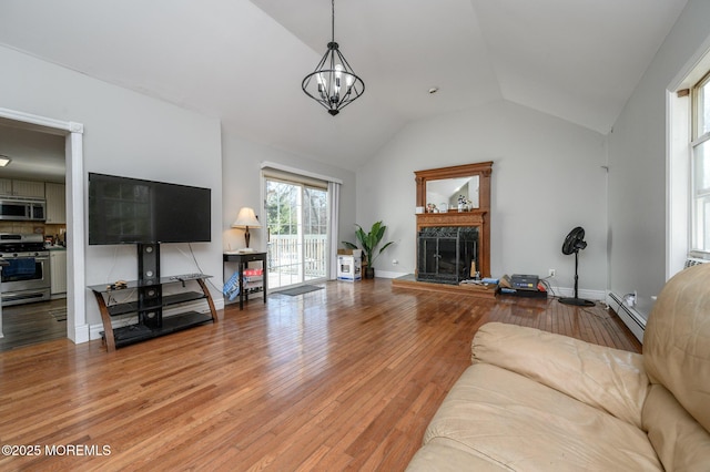 living room with baseboard heating, an inviting chandelier, hardwood / wood-style floors, a fireplace, and vaulted ceiling