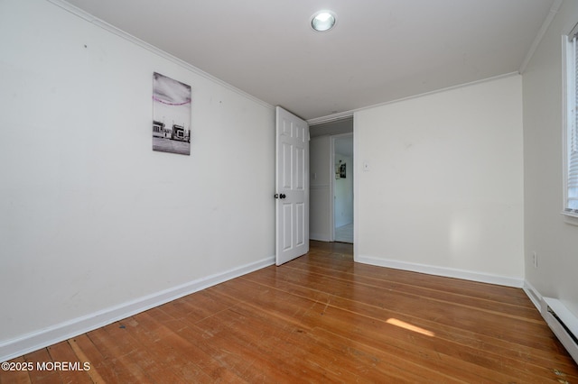 unfurnished room featuring baseboard heating, ornamental molding, and hardwood / wood-style floors