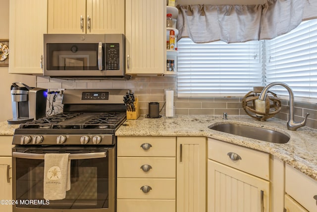 kitchen with backsplash, sink, appliances with stainless steel finishes, cream cabinetry, and light stone counters