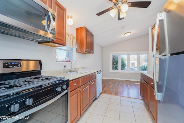 kitchen with lofted ceiling, sink, light tile patterned floors, stainless steel appliances, and light stone countertops