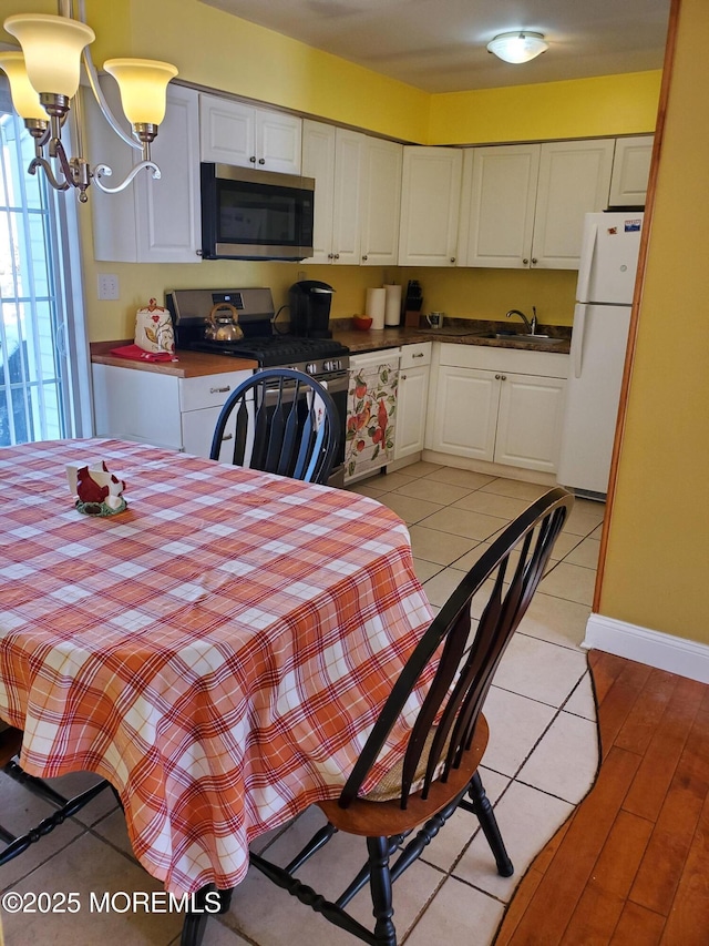 kitchen featuring appliances with stainless steel finishes, light tile patterned flooring, a chandelier, white cabinets, and sink