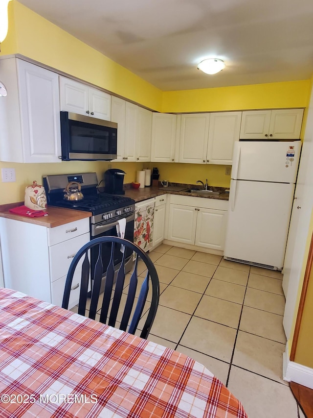 kitchen featuring light tile patterned floors, white cabinets, appliances with stainless steel finishes, and sink