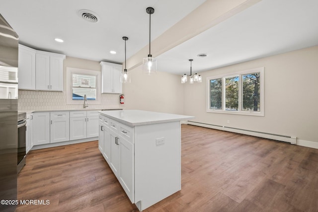 kitchen with baseboard heating, white cabinets, a kitchen island, backsplash, and hanging light fixtures