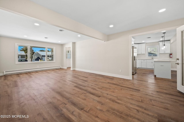 unfurnished living room featuring dark wood-type flooring, baseboard heating, and sink